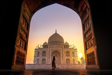 The Taj Mahal at sunset with a woman in silhouette standing in the foreground