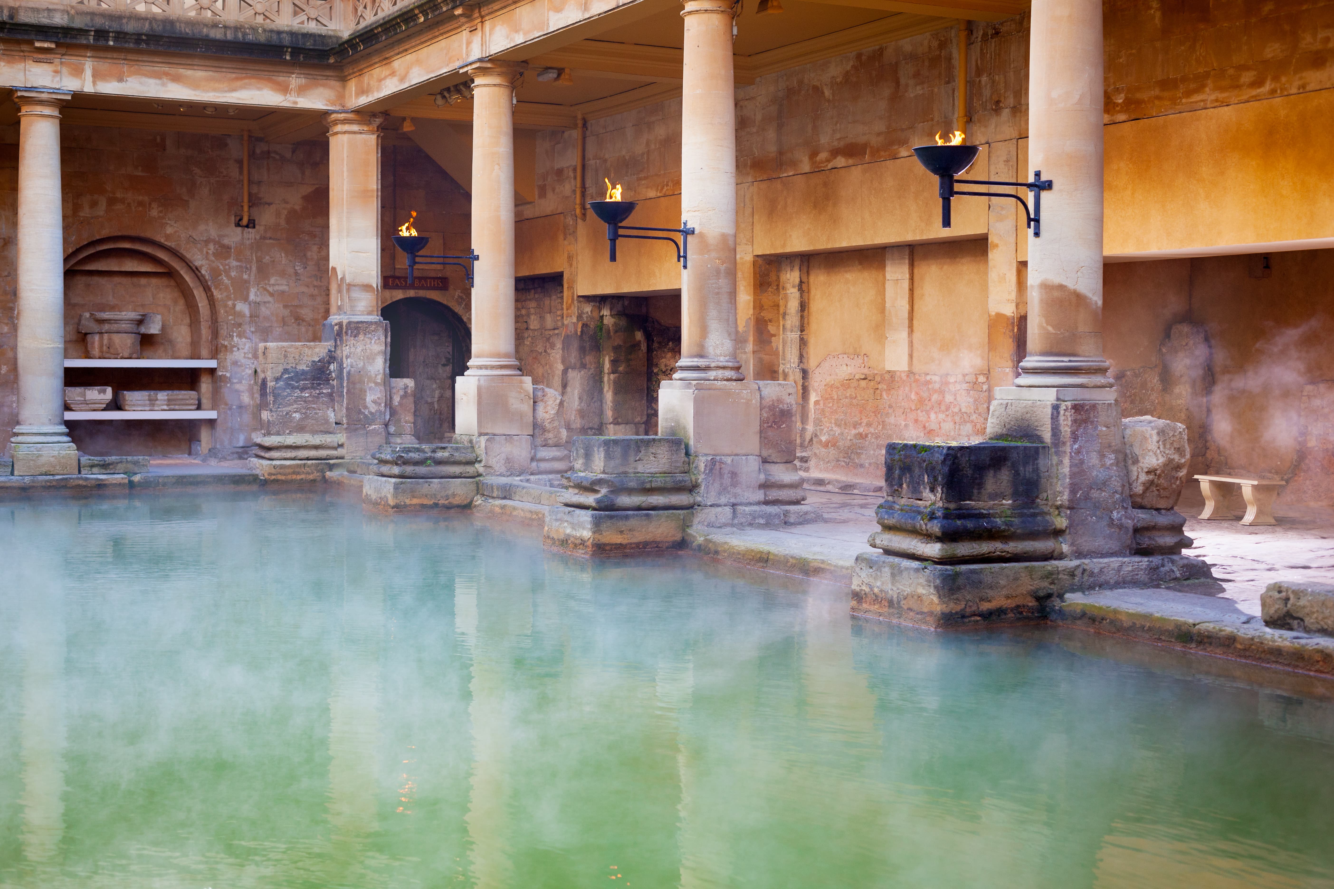 A historic bathhouse scene with green water bath surrounded by pillars