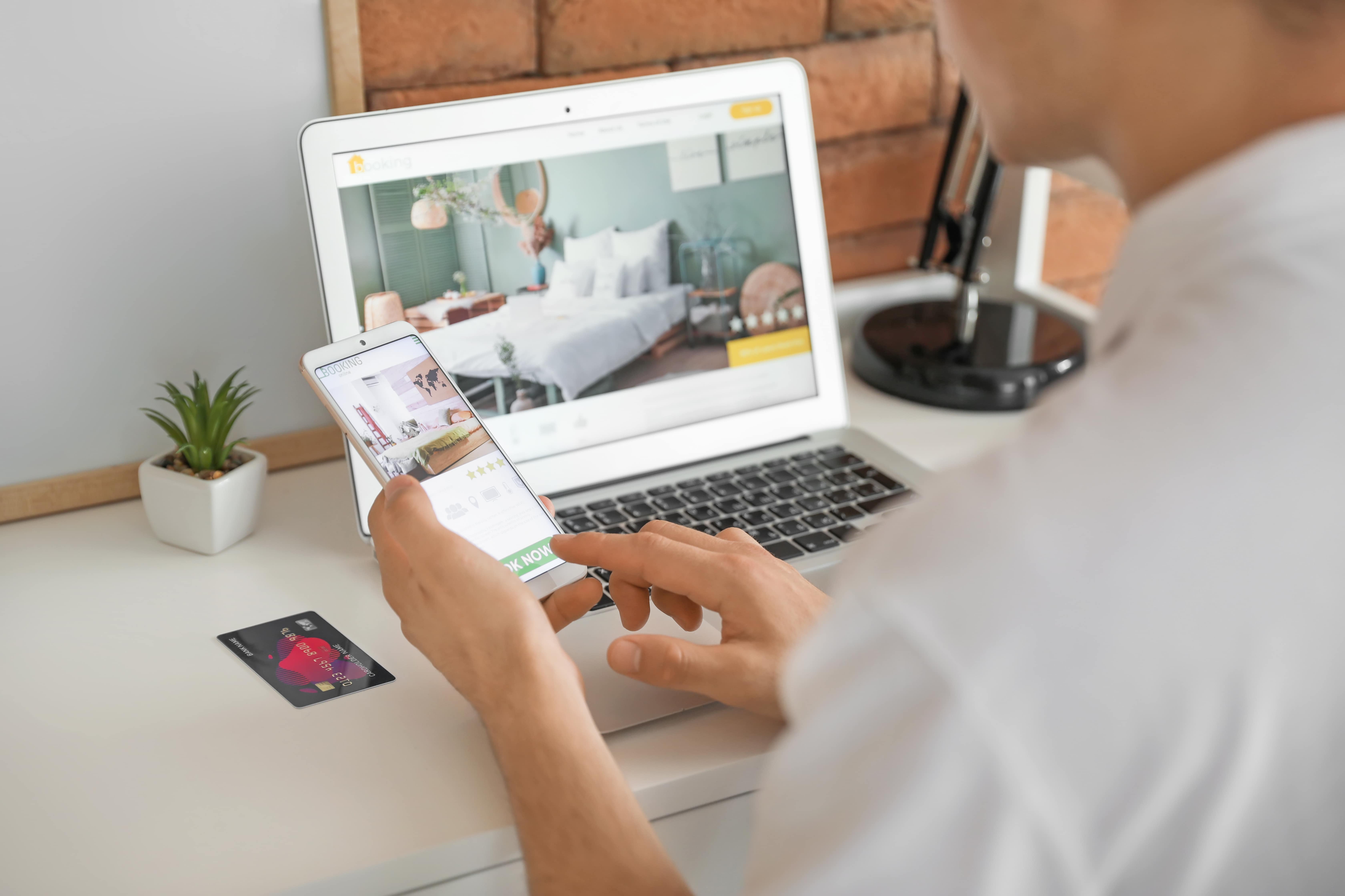 A person booking a hotel on their laptop whilst also researching hotels on another device