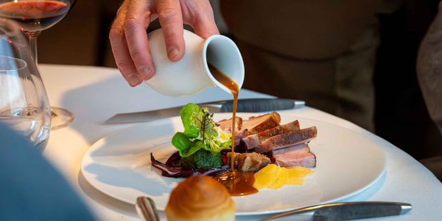 Hand pouring sauce over a meat dish in a gastronomic restaurant