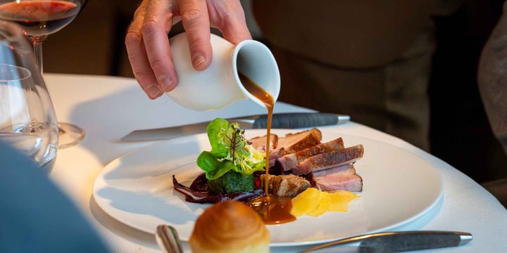 Hand pouring sauce over a meat dish in a gastronomic restaurant