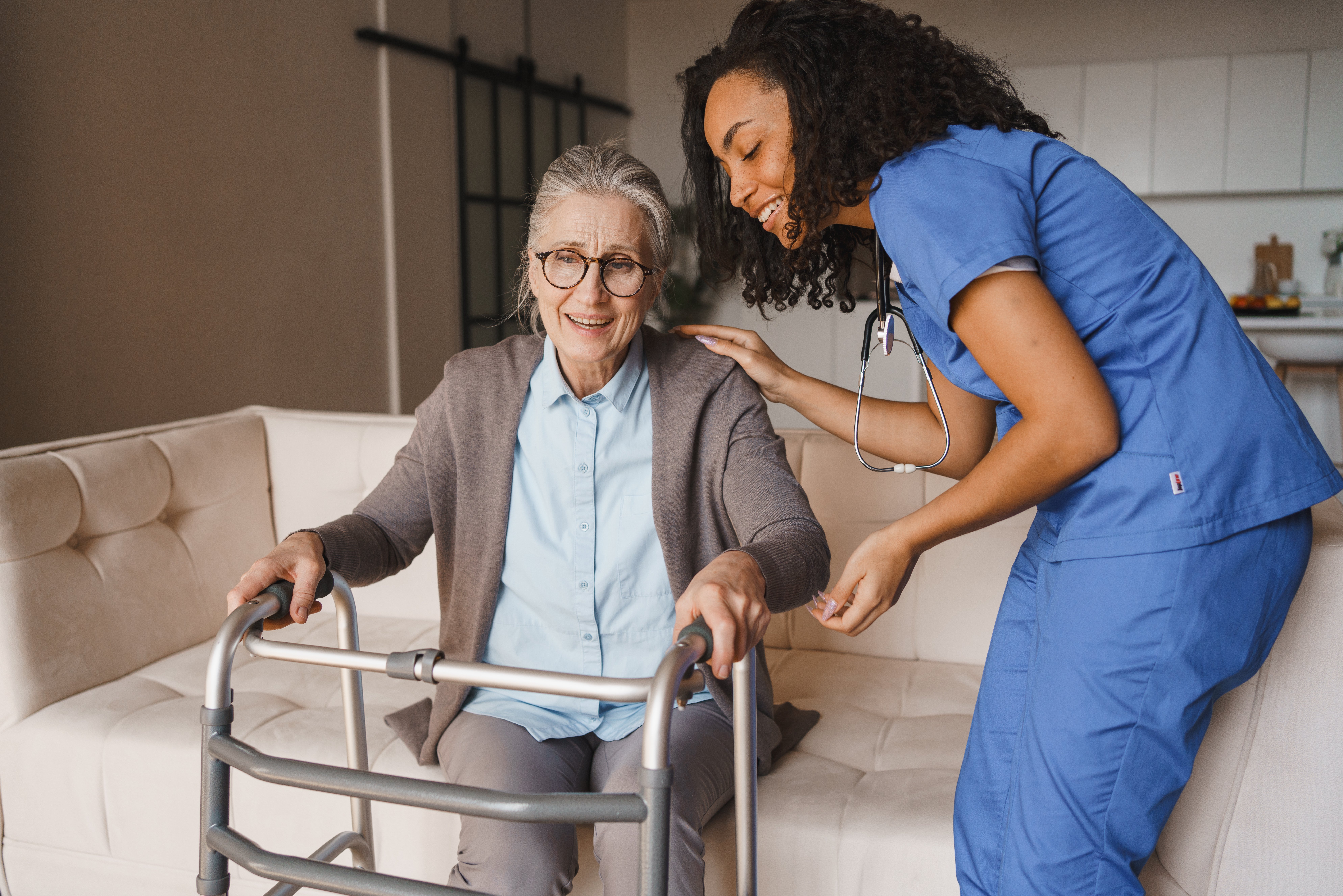 Elderly woman holding onto a Zimmer frame with the support of a nurse