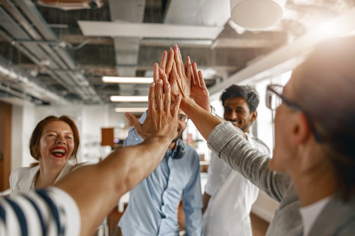 Team members joining hands in a high-five during a collaborative workplace meeting, symbolizing trust, teamwork and high performance.