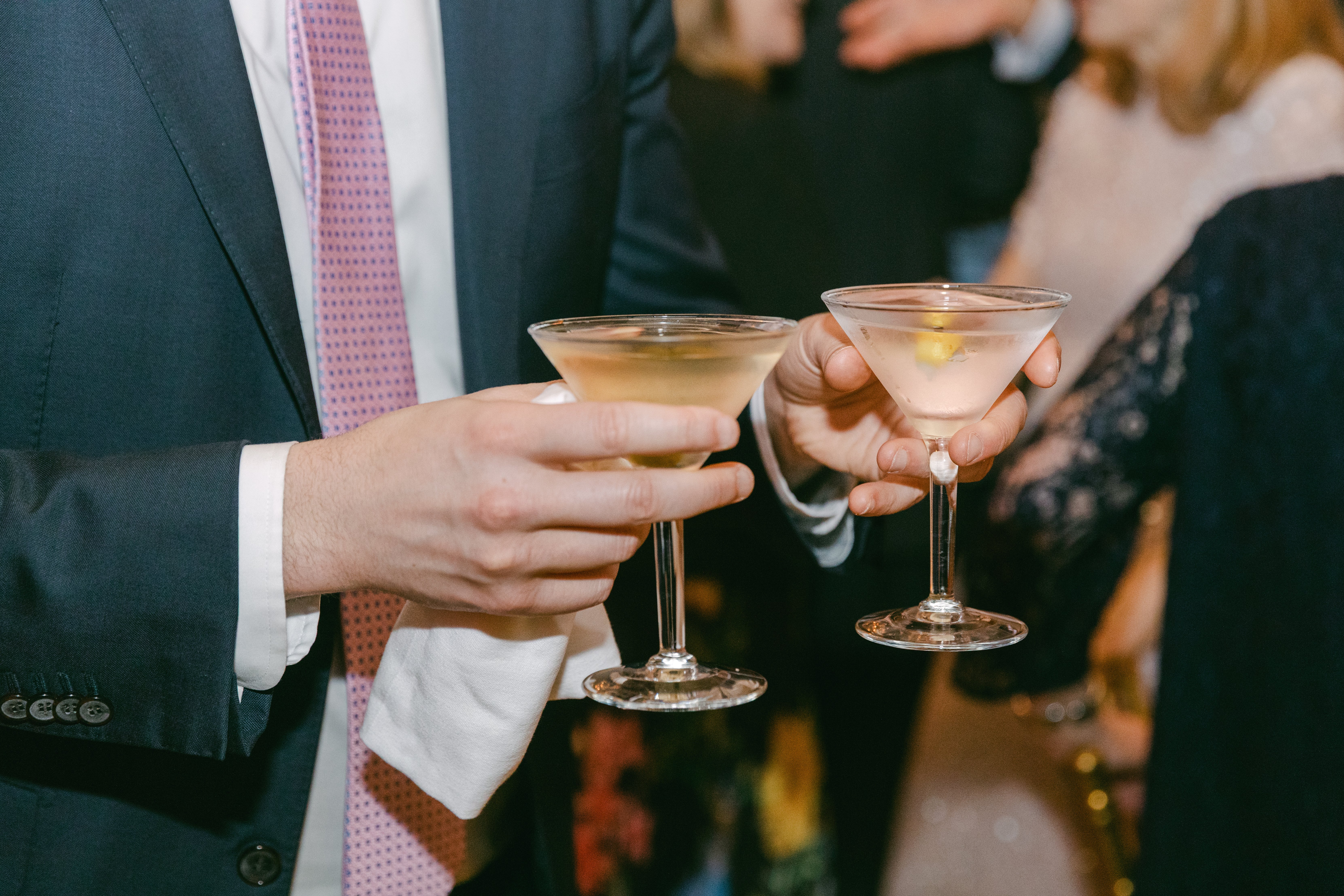 Two martini cocktails held by a man in a suit at a social gathering