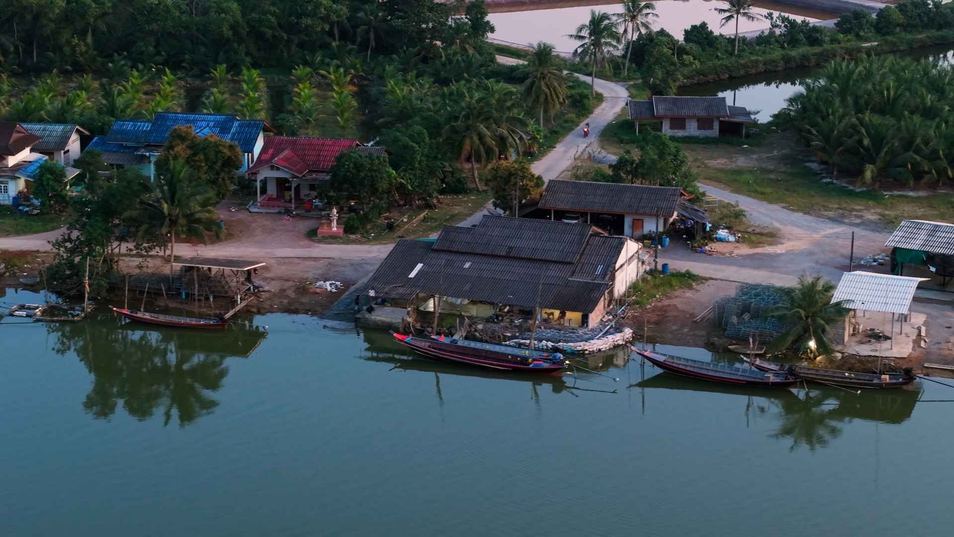 Aerial view of riverside village with boats and local homes surrounded by tropical nature and waterway.
