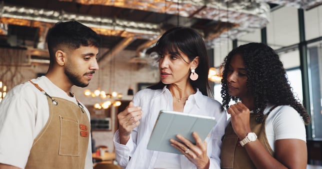 A manager speaking to two employees about restaurant staff scheduling, holding an iPad