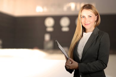 A blonde, female hotel manager, wearing a black suit and white blouse is holding a file in her hands