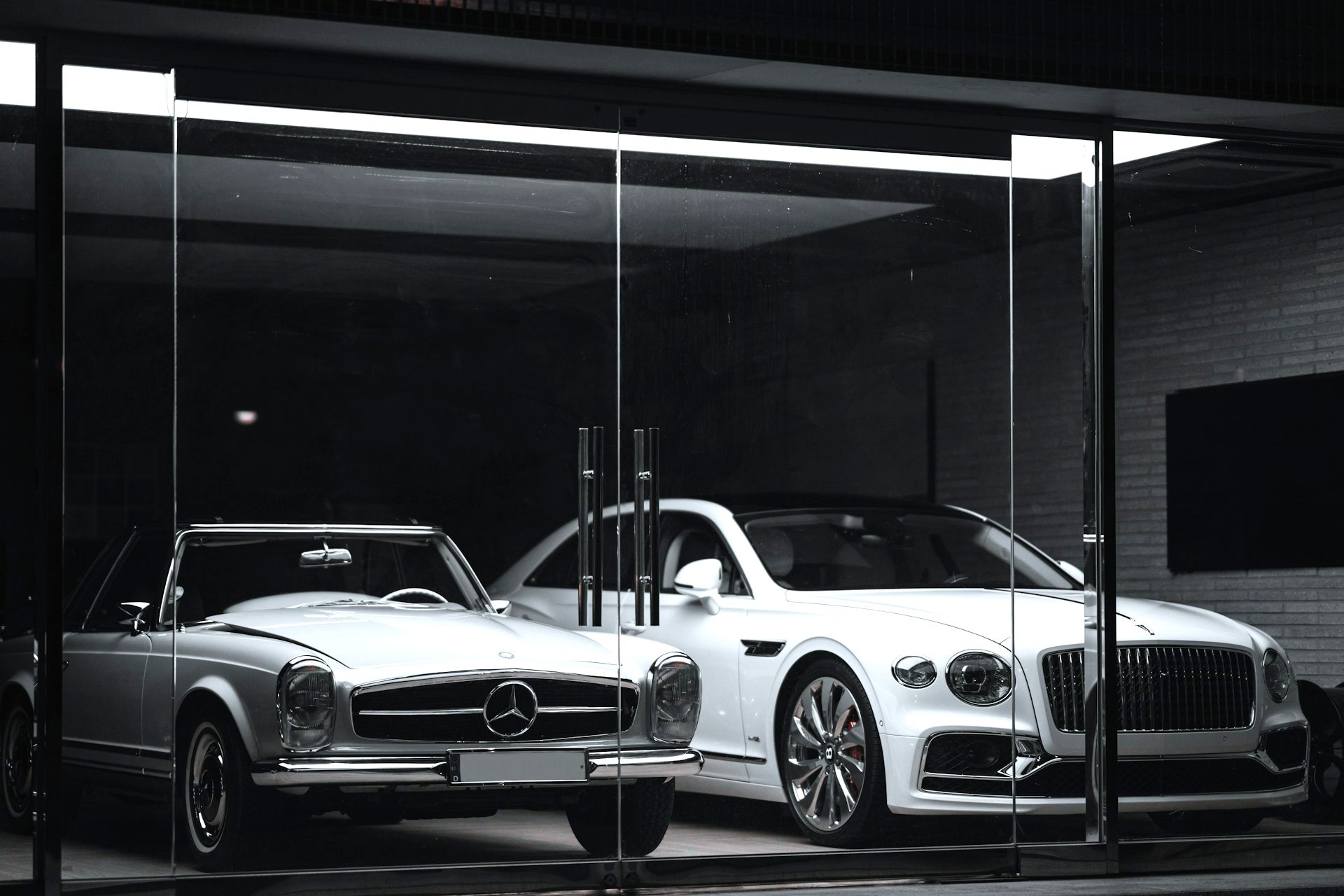 A white Bentley Continental GT parked next to a Mercedes Benz 300SL Roadster