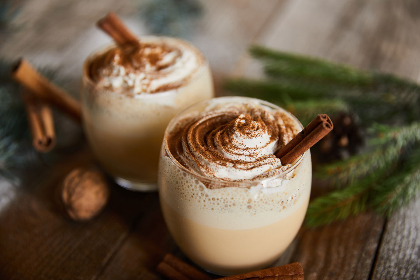 2 glasses of Eggnog on a table with pine branch